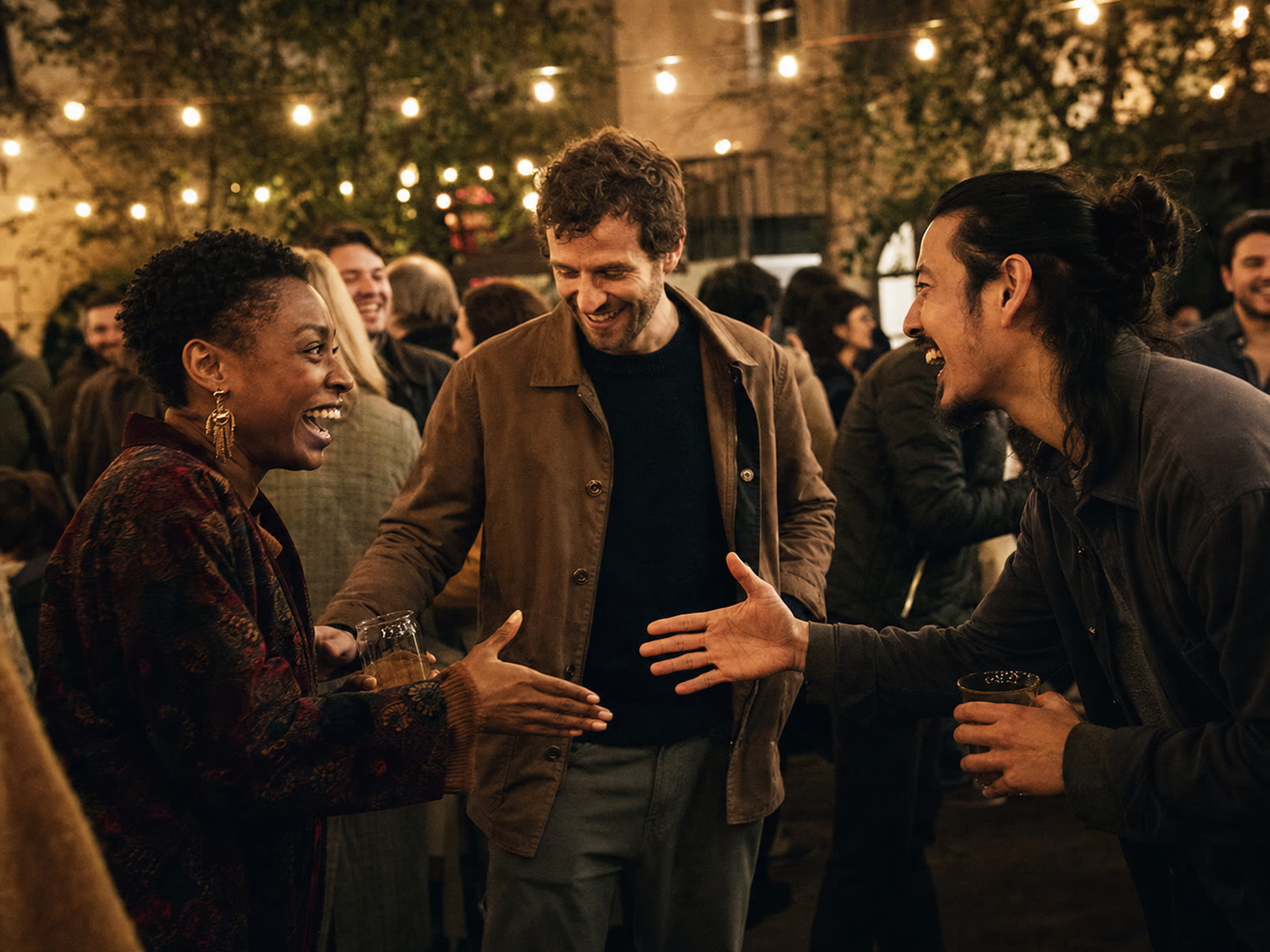 A host introducing two delighted guests at a crowded evening gathering